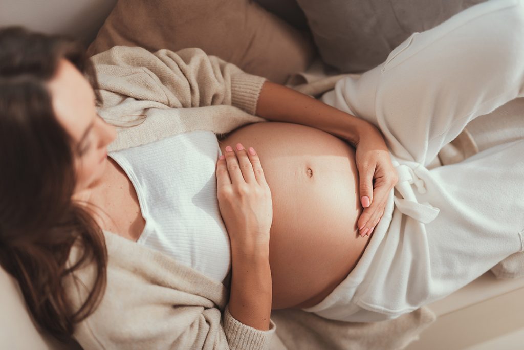 Careless lady lying and holding her hands on pregnant belly Careless lady lying and holding her hands on pregnant belly